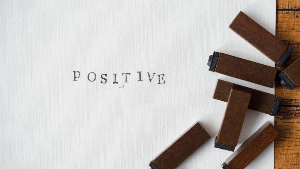 Close-up of 'Positive' word created with vintage wooden letter stamps on textured paper.